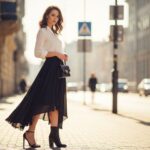 Mladá žena stojící ve městě s asymetrickou sukní a různými druhy obuvi na jedné noze.