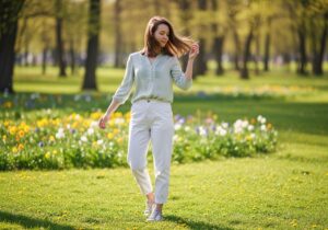 Mladá žena v jarním oblečení stojí v květinovém parku za slunečného dne.