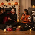 Skupina mladých lidí v obýváku připravuje kostýmy na Halloween s dekoracemi a dýněmi.